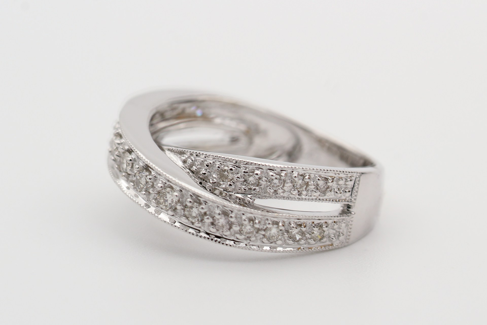 A split shank white gold fashion ring displayed on a white surface. A split shank white gold fashion ring displayed on a white surface.