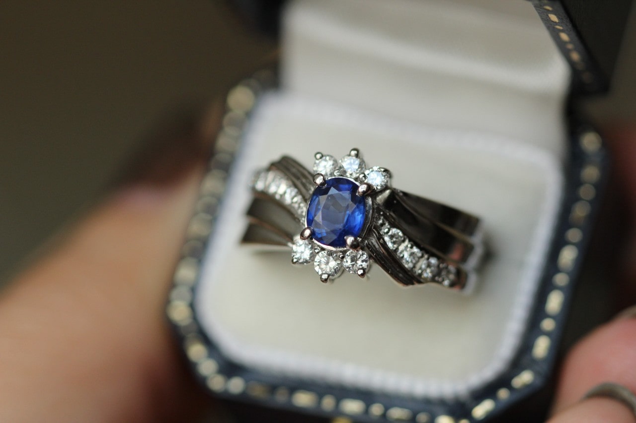 A sapphire and diamond cluster ring with a split shank band displayed in a jewelry box. A sapphire and diamond cluster ring with a split shank band displayed in a jewelry box.